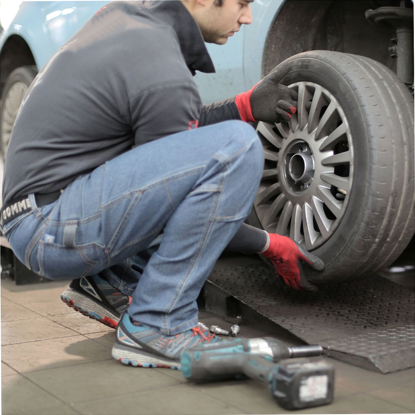 Technician taking a grey alloy off a light blue car in a workshop