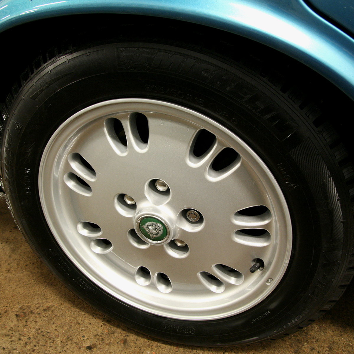 Silver painted Jaguar alloy on a light blue car